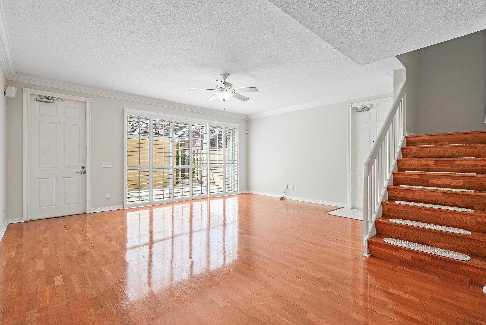 Empty living room with glossy wood floors, large shuttered windows, and a wooden staircase.
