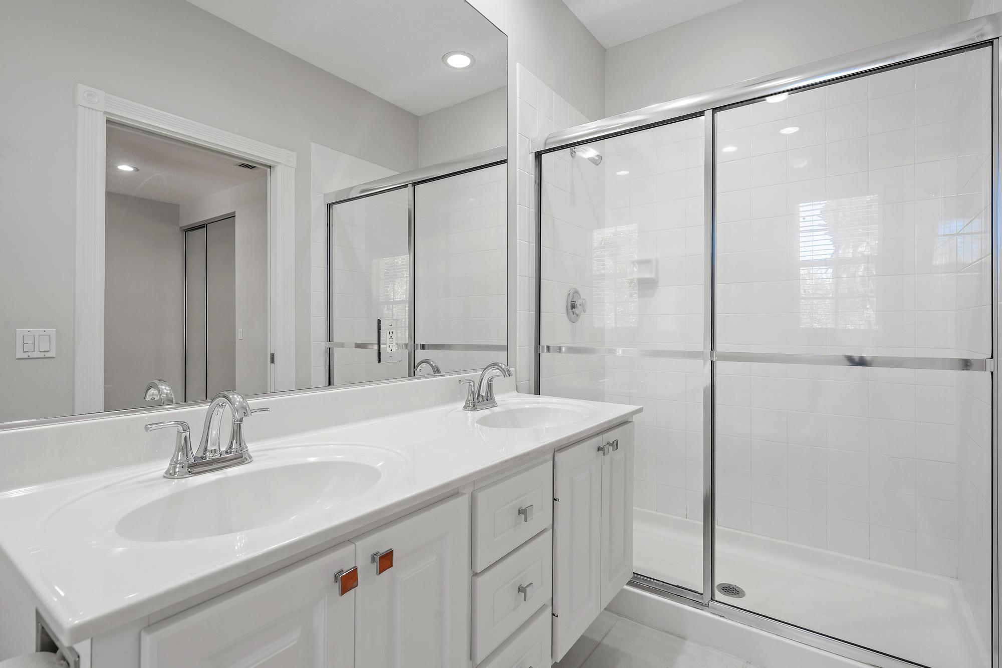 Bathroom with a double-sink vanity and a glass-enclosed tiled shower.