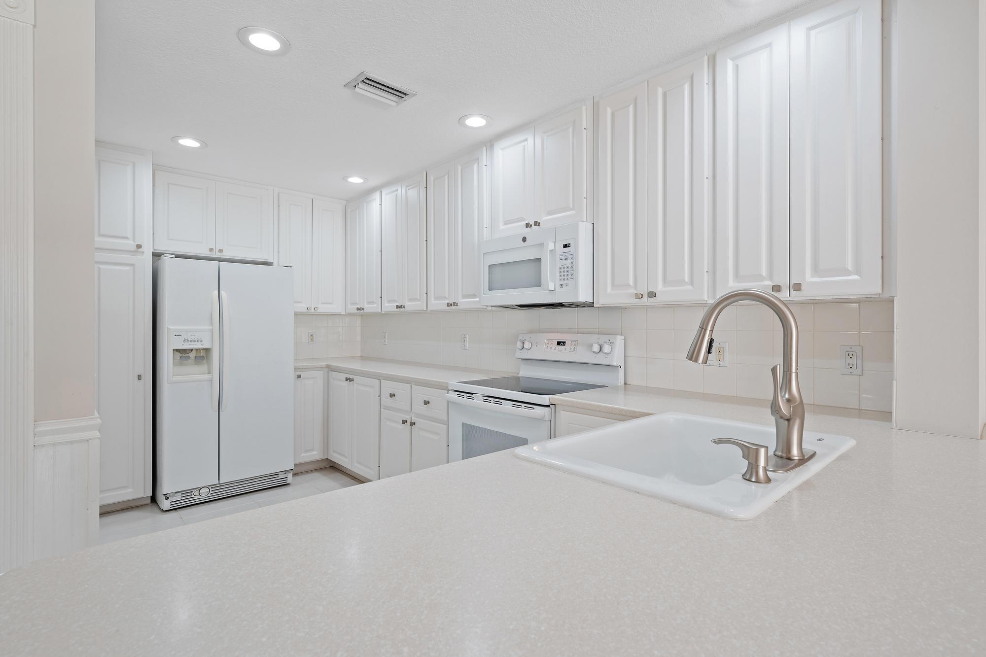 White kitchen with paneled cabinets, white appliances, and a foreground sink with a curved faucet.