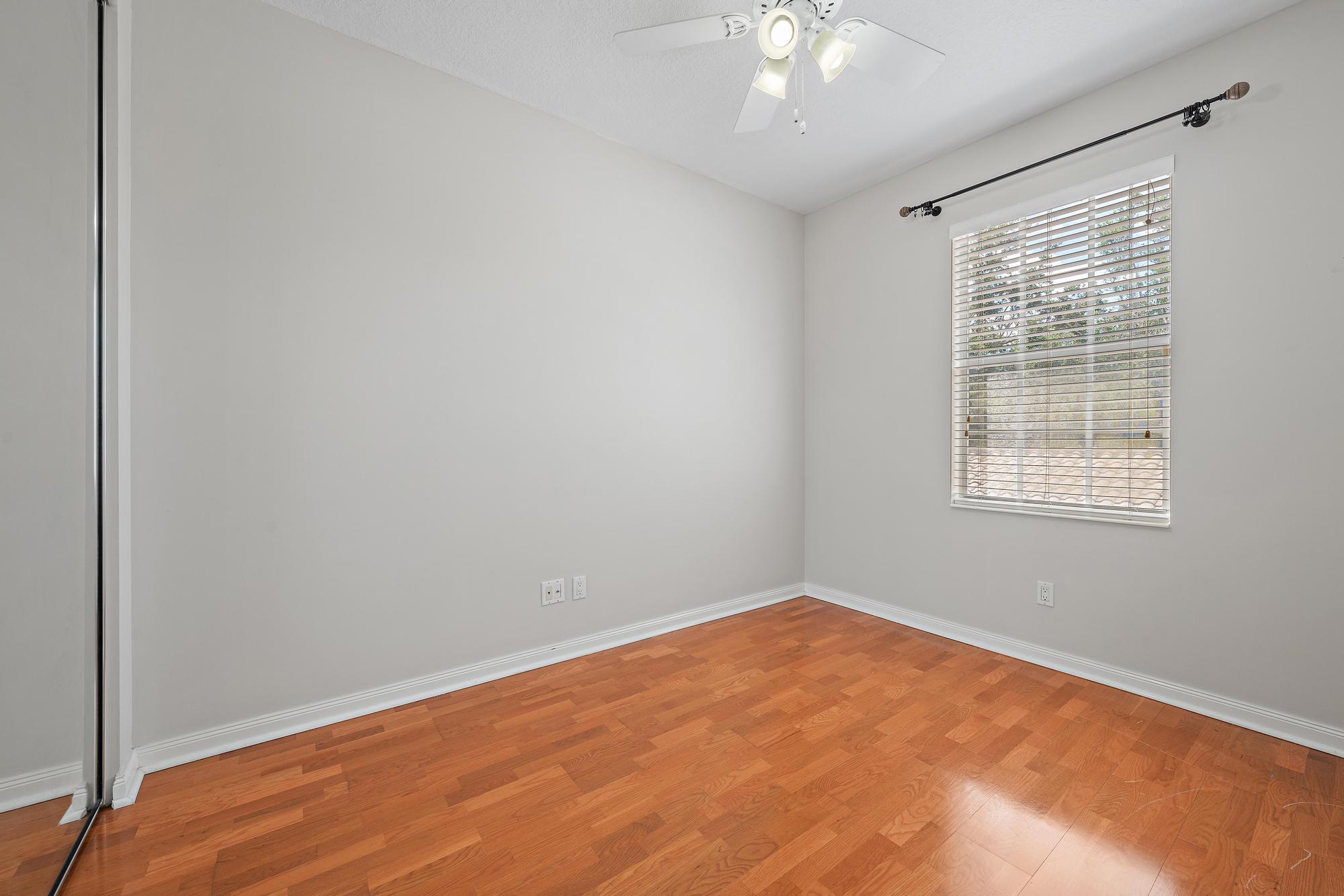 Vacant bedroom with hardwood floors, a ceiling fan, and a window with white blinds.