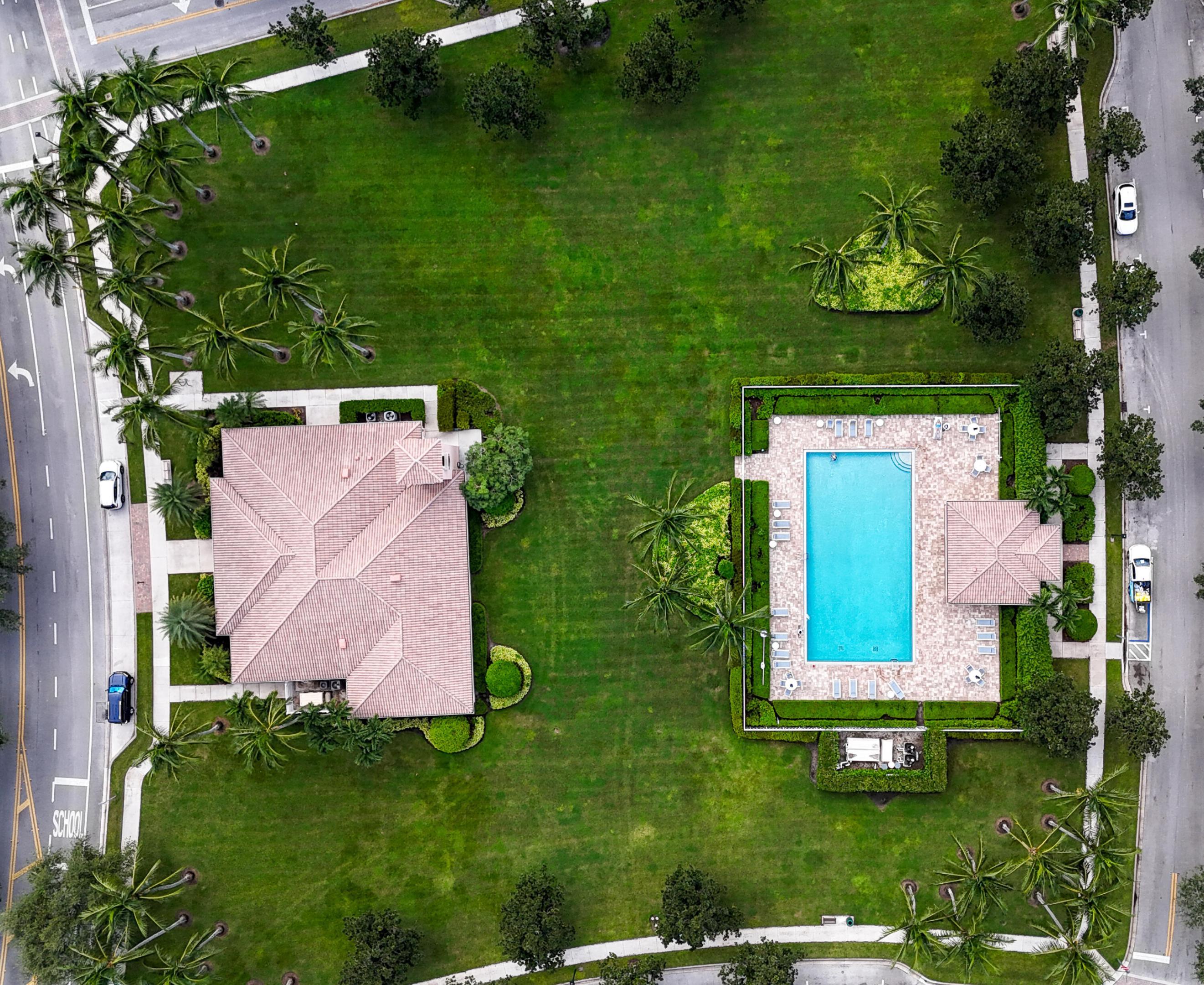 Aerial view of a tile-roofed home, broad lawn, and rectangular pool with a paved deck.
