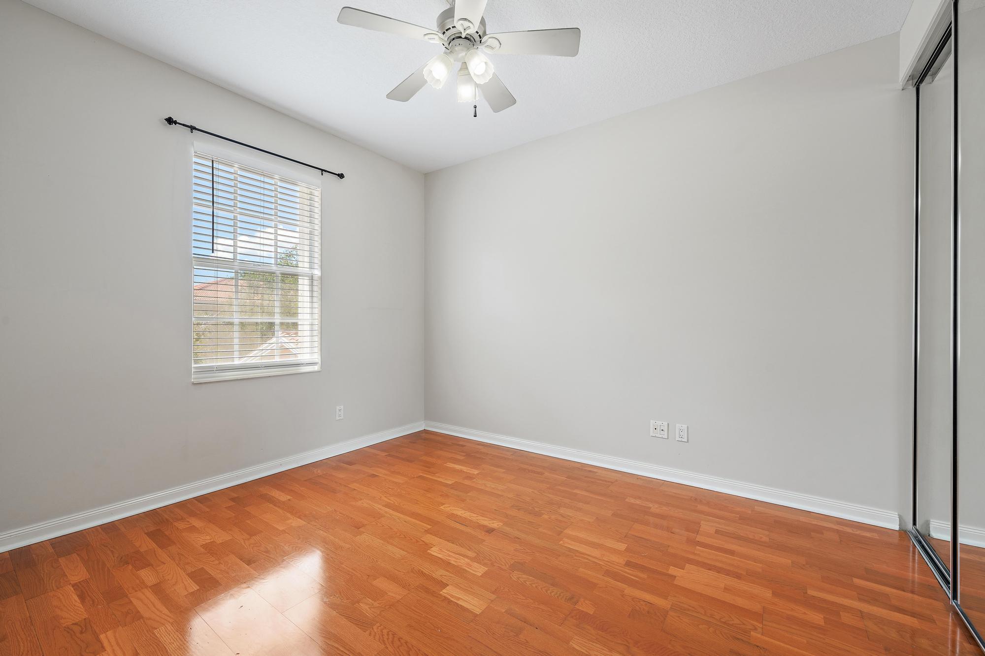 Empty bedroom with hardwood floors, a ceiling fan, and mirrored sliding closet doors.