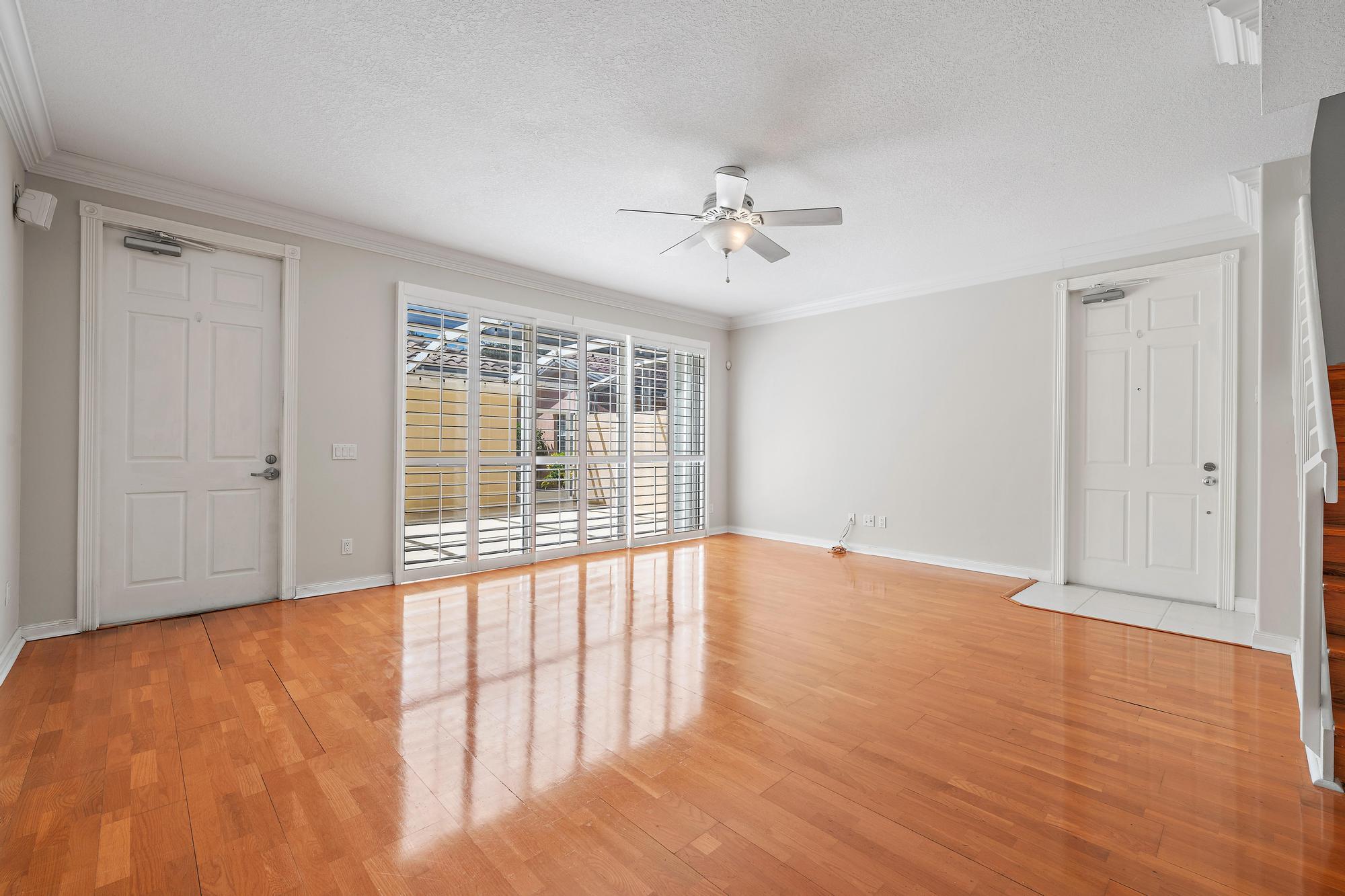 Empty room with glossy hardwood floors, plantation-shuttered windows, and a ceiling fan.