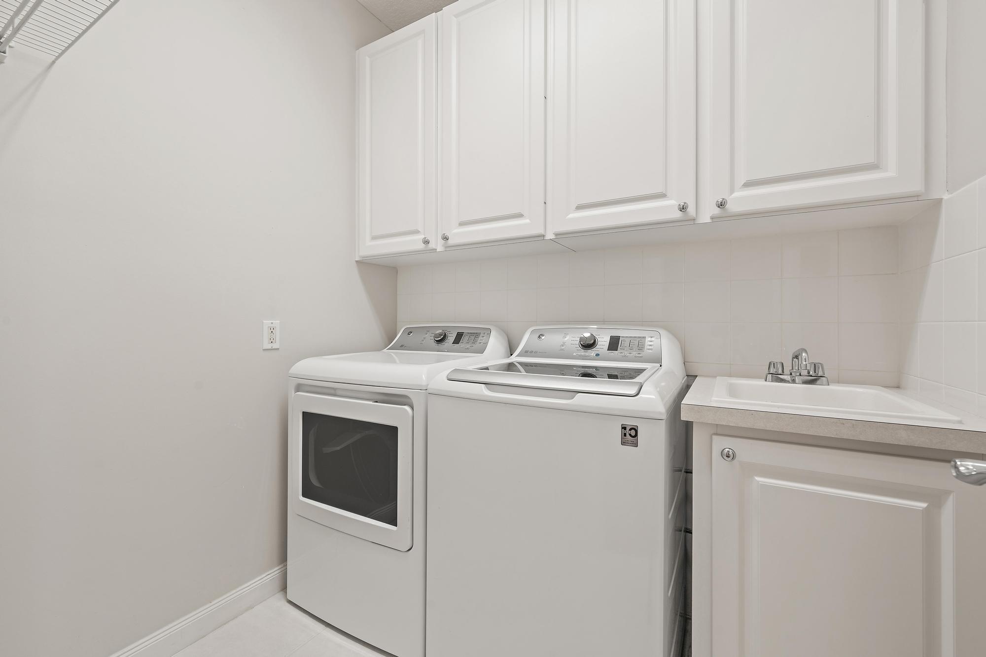Laundry room with a white washer and dryer, overhead cabinets, and a utility sink.