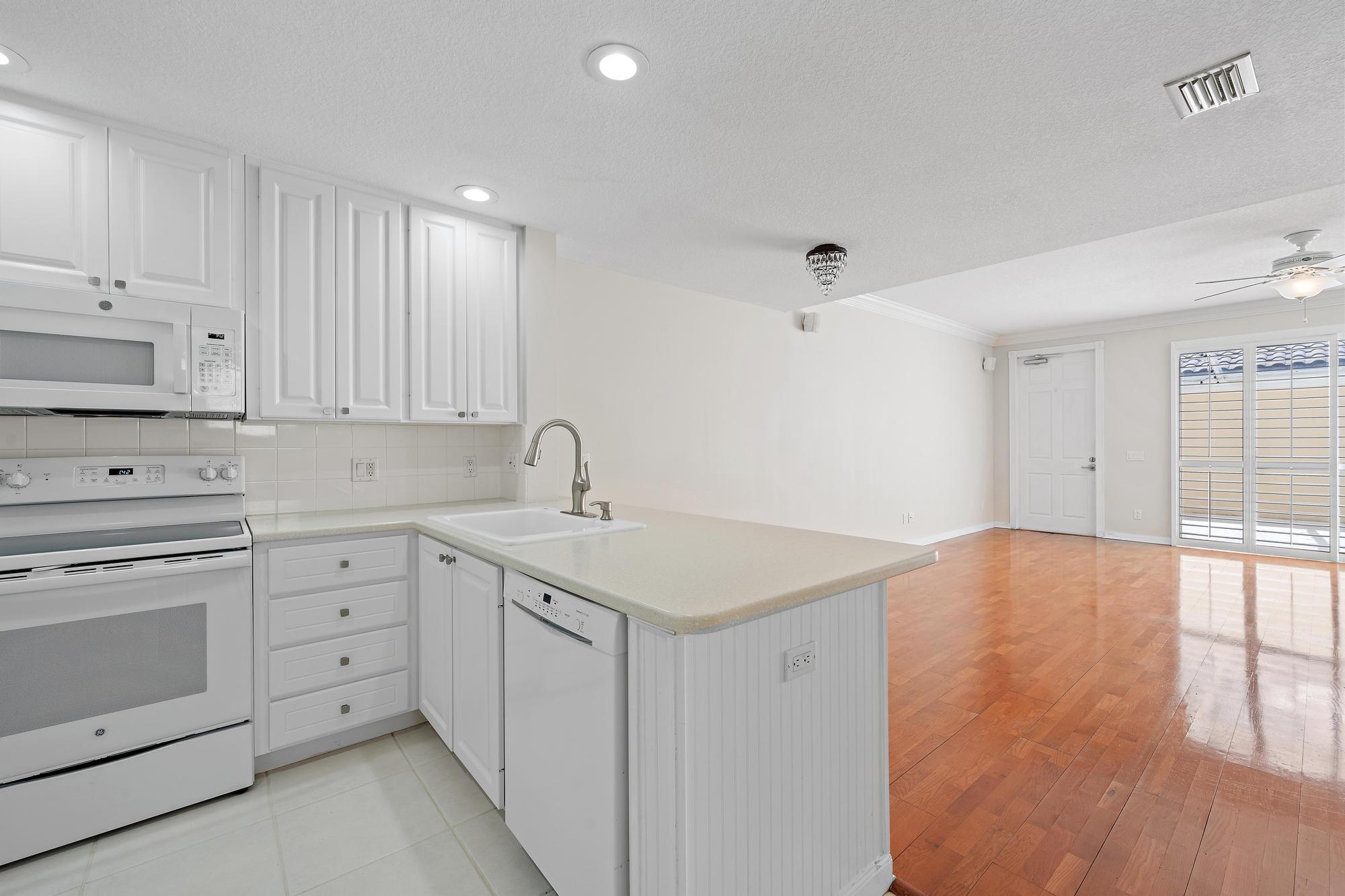 Vacant kitchen with white cabinets and a sink peninsula opening onto a hardwood-floored living area.