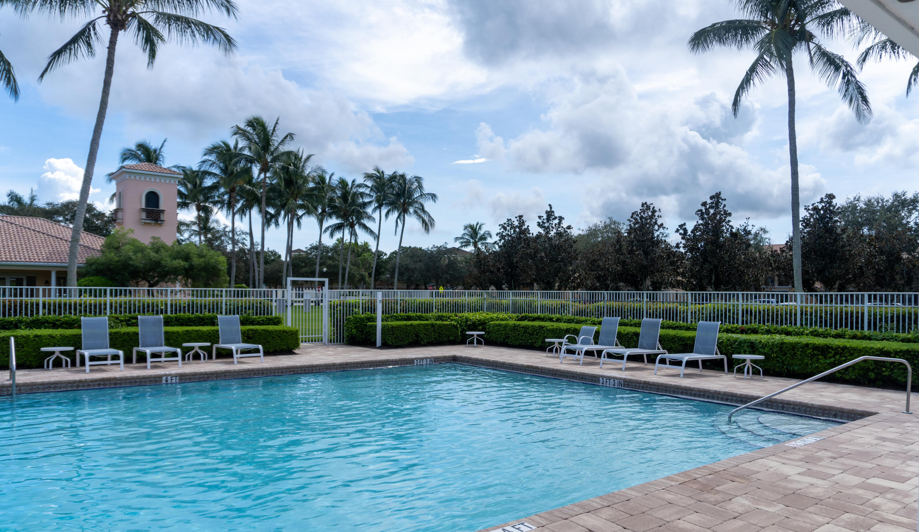 Outdoor swimming pool with turquoise water, tiled deck, lounge chairs, and palm trees.