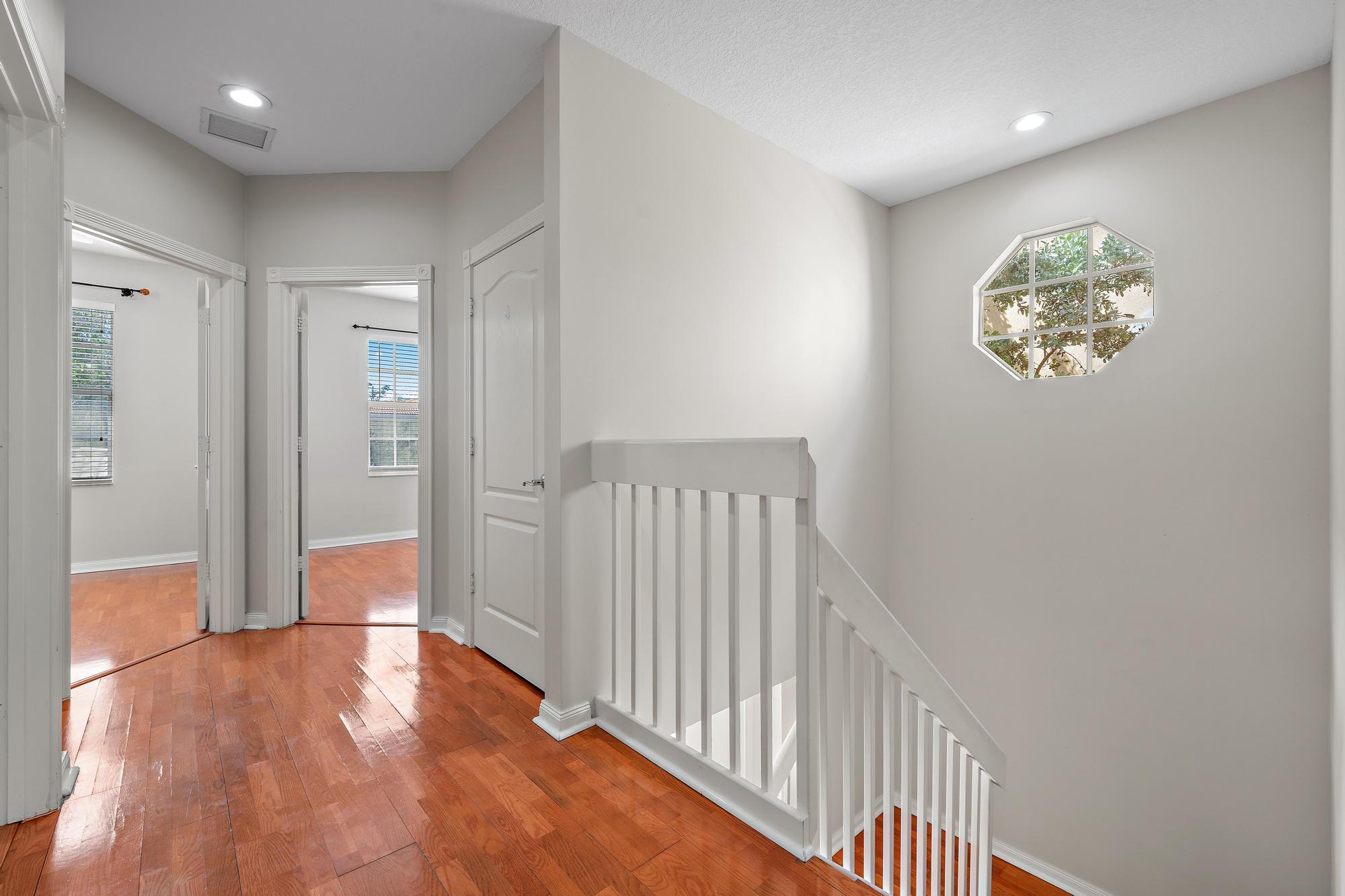 Upstairs hallway with hardwood floors, a white stair railing, and an octagonal window.