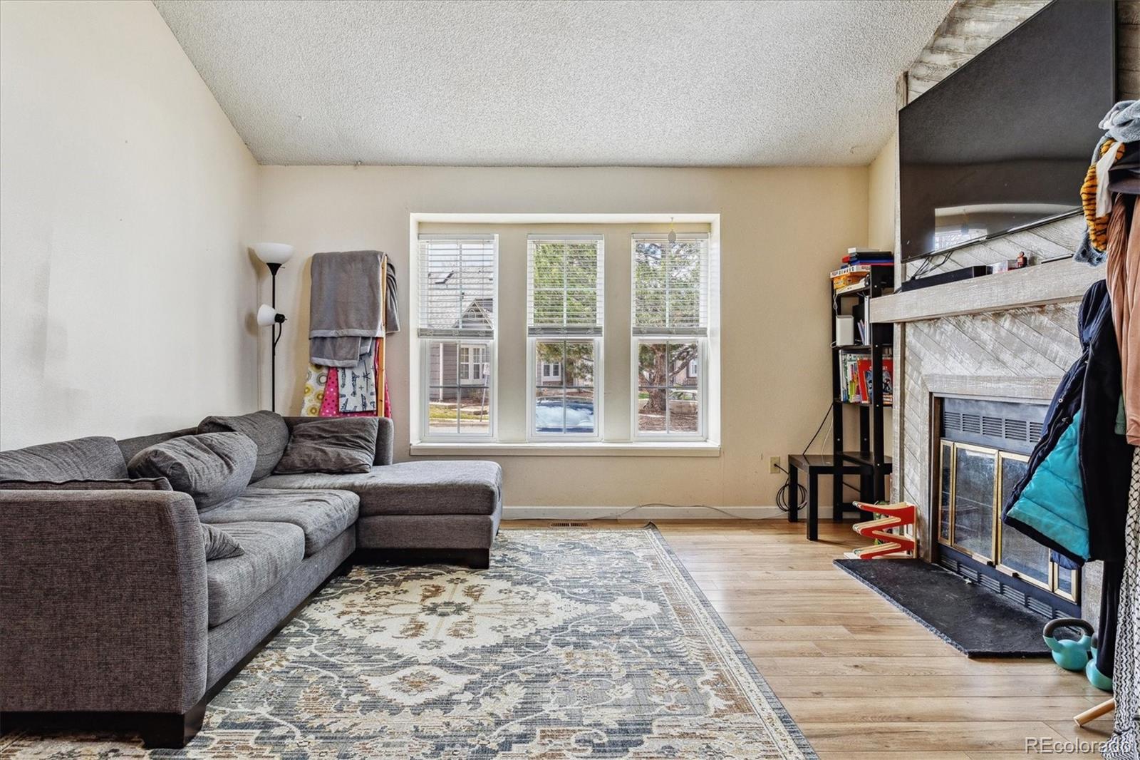 Living room with a gray sectional, patterned rug, three windows, and a stone fireplace.