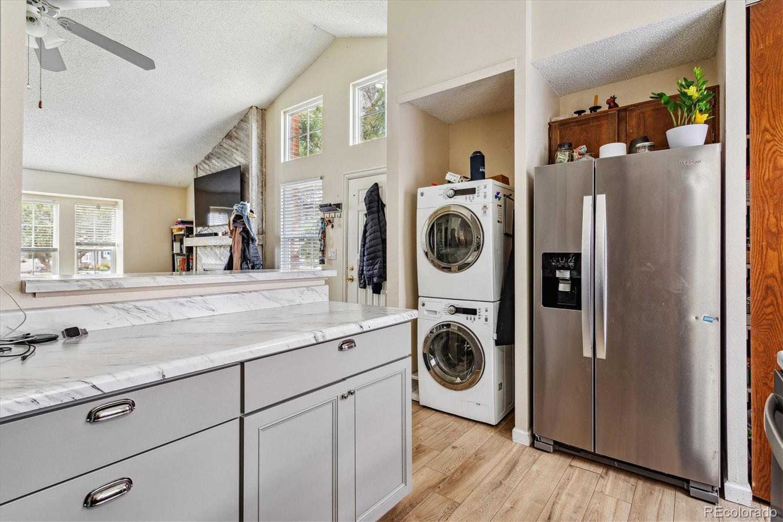 Kitchen with a marble-look island, stainless refrigerator, and stacked washer and dryer.