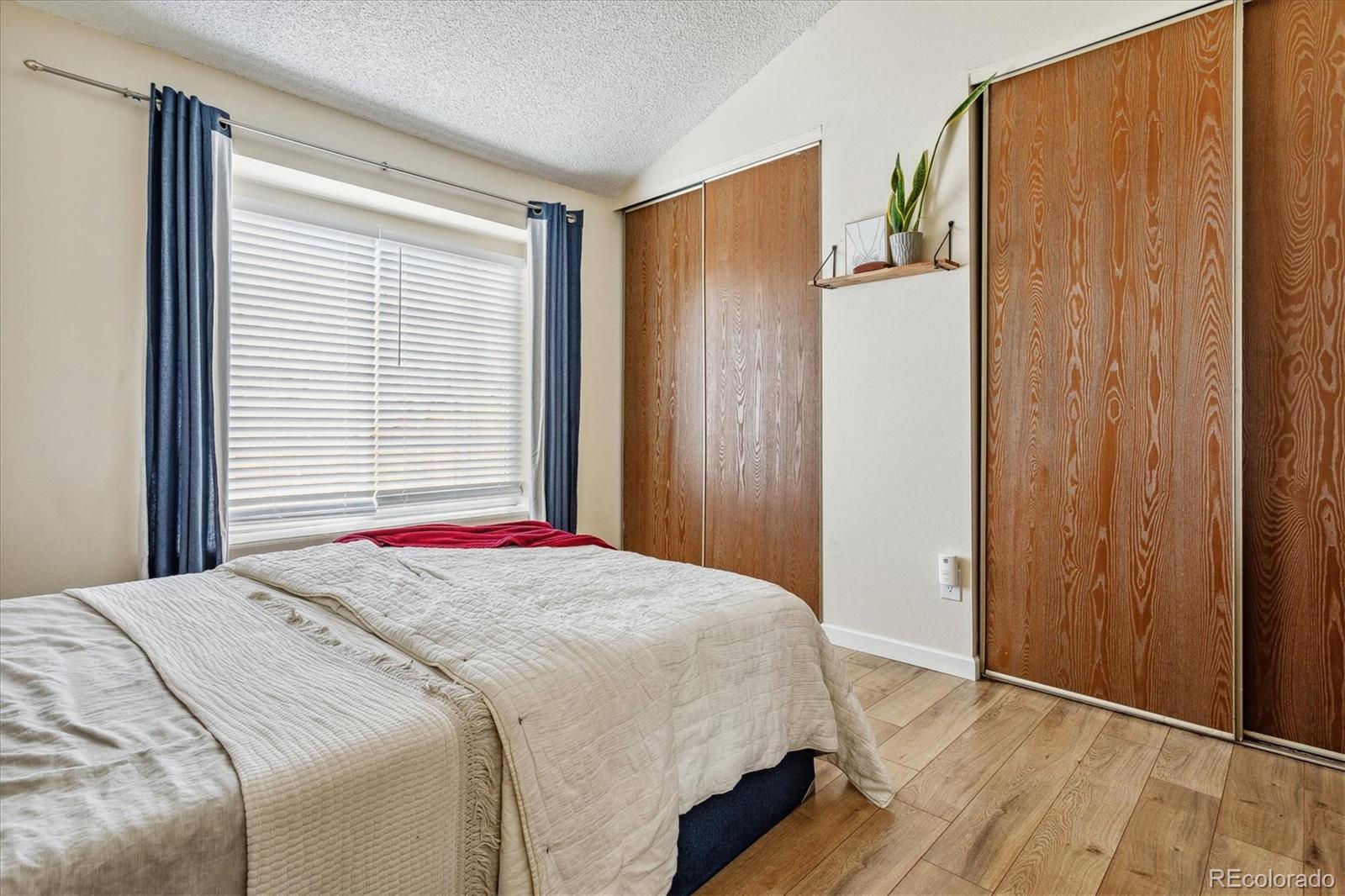Bedroom with a white-quilted bed, wooden sliding closet doors, and a window framed by navy curtains.