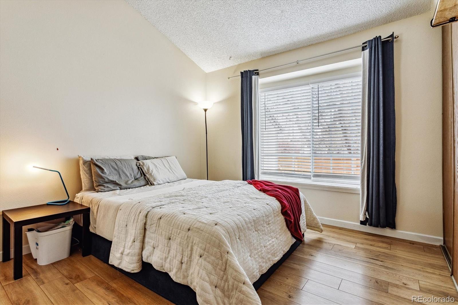 Bedroom with a cream-quilted bed, red throw, and window framed by dark curtains.