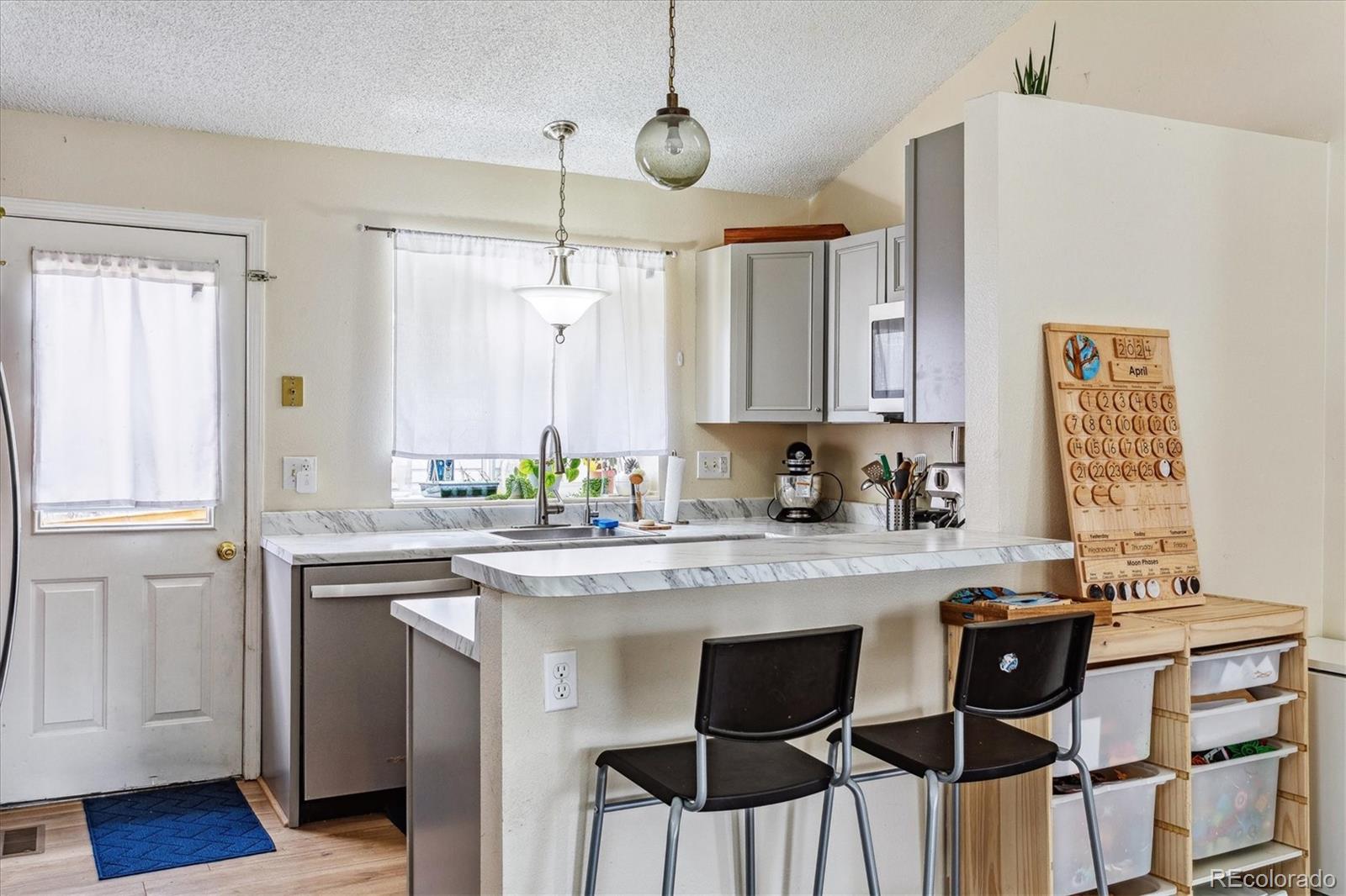 Kitchen with gray cabinets, marble-look counters, a sink beneath a curtained window, and a raised breakfast bar.