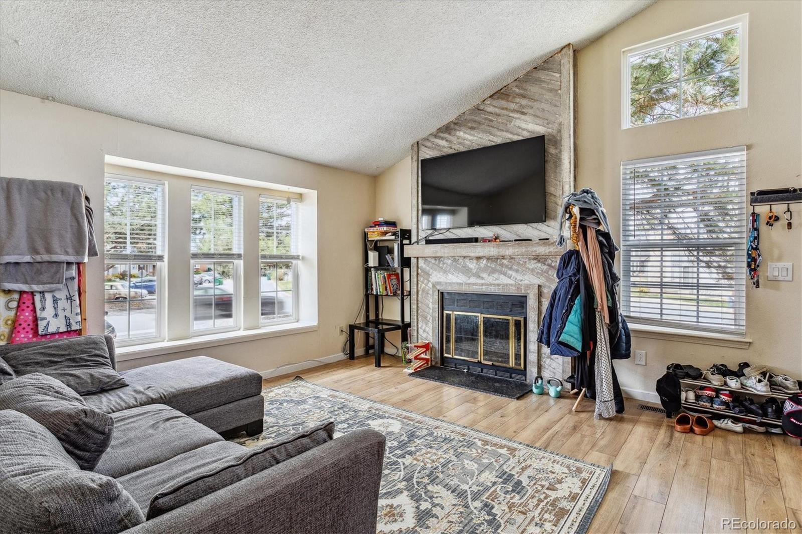 Living room with a stone fireplace, mounted television, gray sectional, and multiple windows.