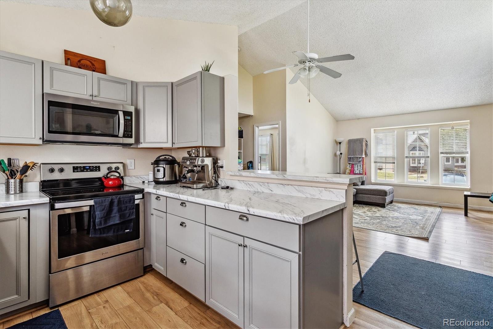 Kitchen with gray cabinets and stainless appliances opening to a bright living area.