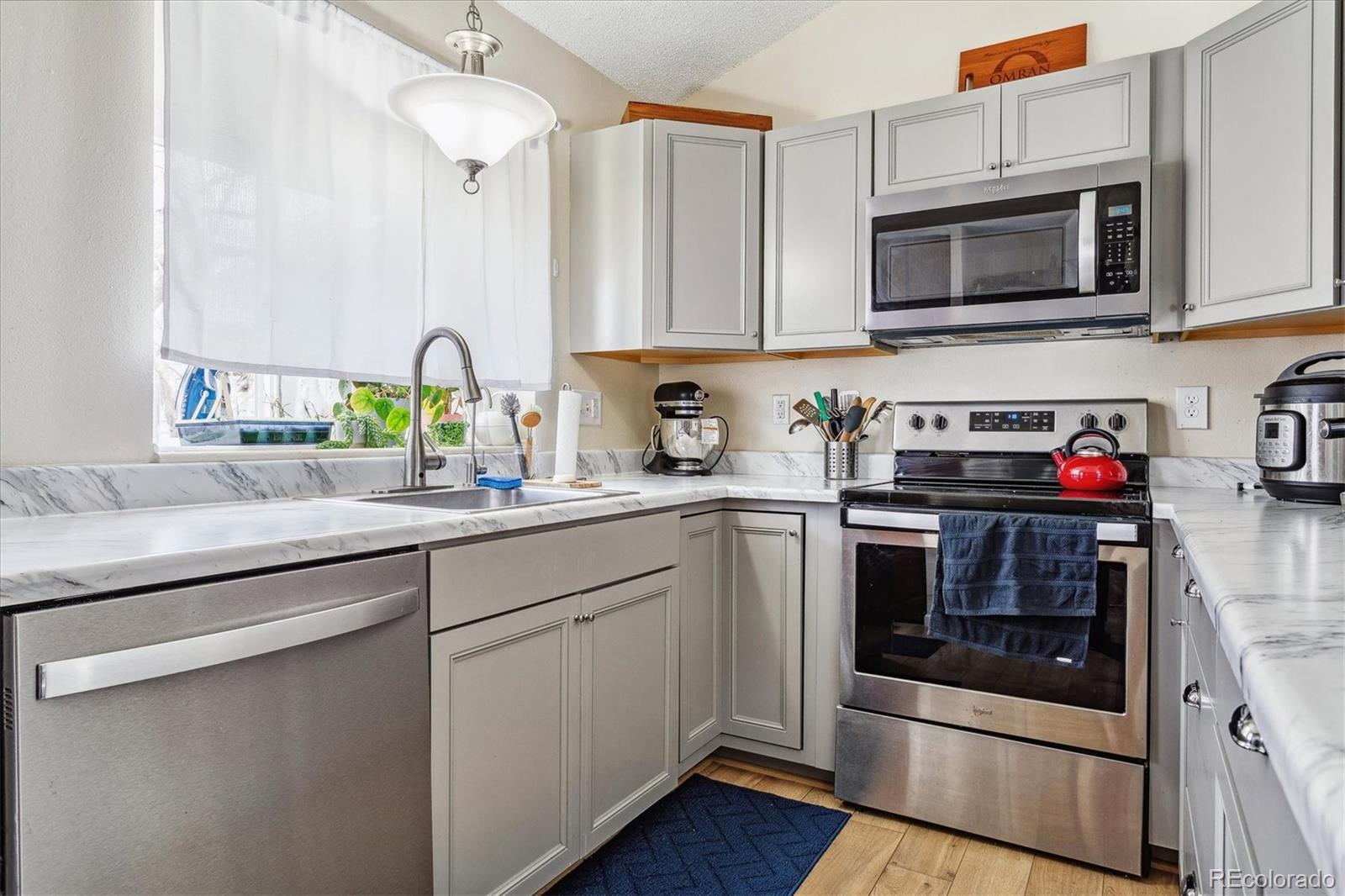 Kitchen with white cabinets, marble-look counters, stainless steel appliances, and a sink beneath a window.