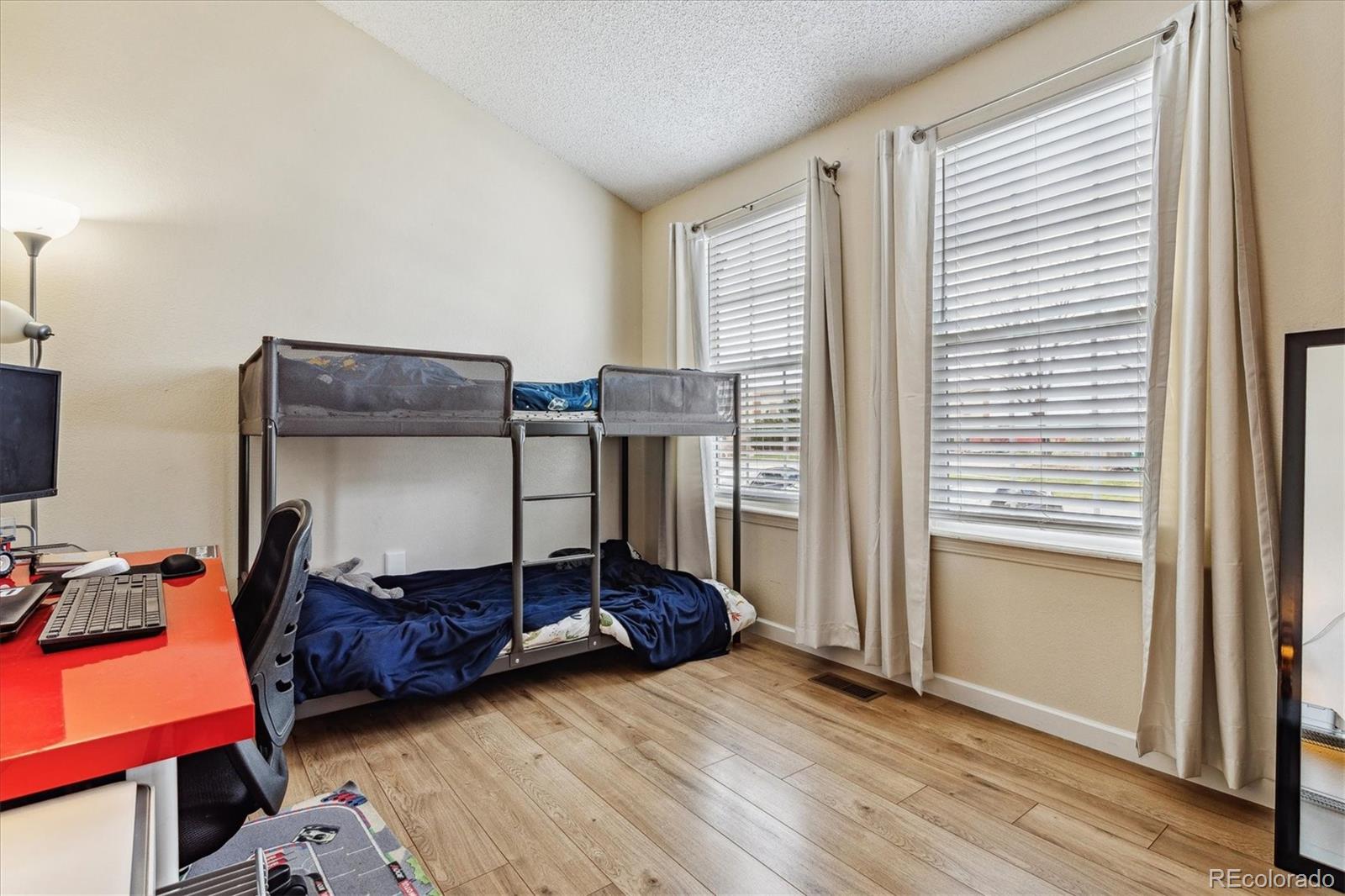 Bedroom with a metal bunk bed, navy bedding, red desk, and two curtained windows.