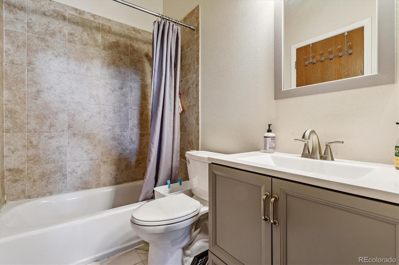 Bathroom with tiled tub surround, gray shower curtain, toilet, and taupe vanity.