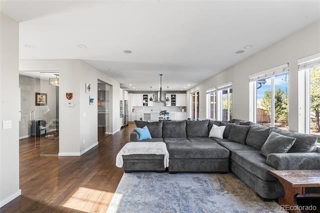 Open-plan living room with a large gray sectional, dark wood floors, and windows overlooking greenery.