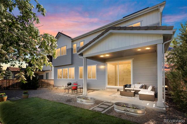 Two-story gray home with a covered patio and outdoor seating at dusk.