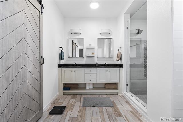 Bathroom with double vanity, black countertop, glass shower, and gray herringbone sliding door.