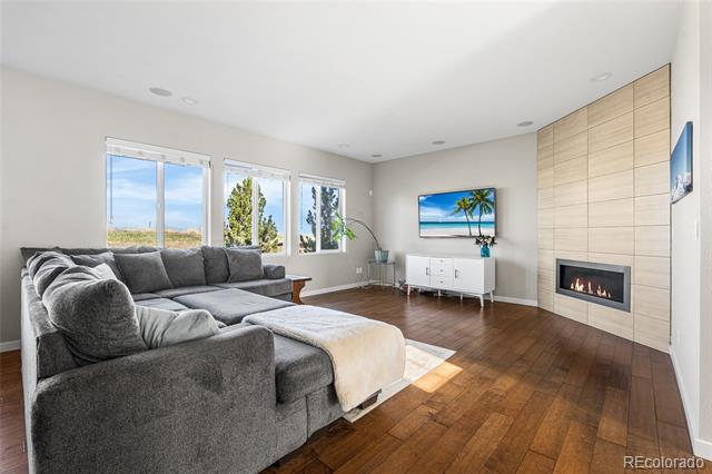Living room with a gray sectional, wood floors, and a linear fireplace in a light wood feature wall.