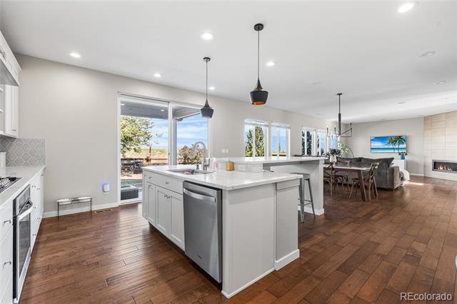 Open-plan kitchen with a large white island, stainless steel dishwasher, and hardwood floors.