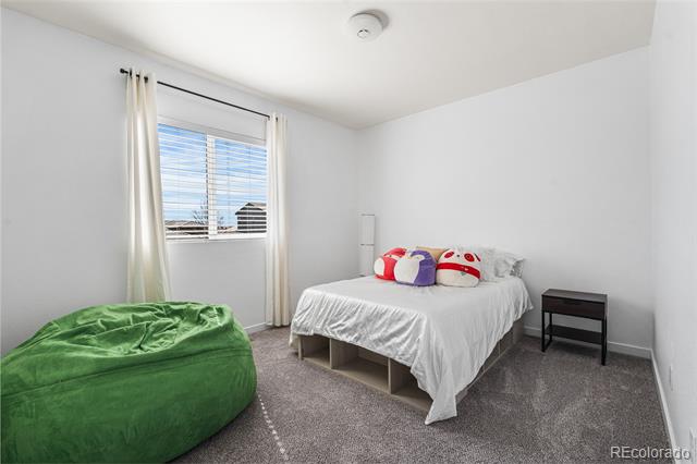 Bedroom with a white bed, colorful pillows, green beanbag chair, and curtained window.