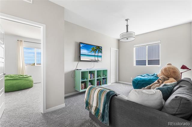 Staged bonus room with a gray sofa, oversized teddy bear, turquoise beanbag, and wall-mounted television.
