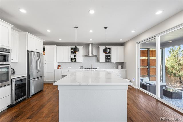 Modern white kitchen with a large island, stainless steel appliances, and sliding glass doors to a patio.