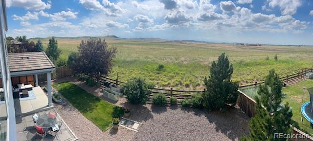 Panoramic view across a fenced backyard and patio to open fields.