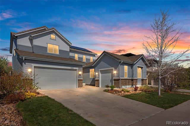 Gray two-story house with attached garages and a wide driveway under a colorful dusk sky.