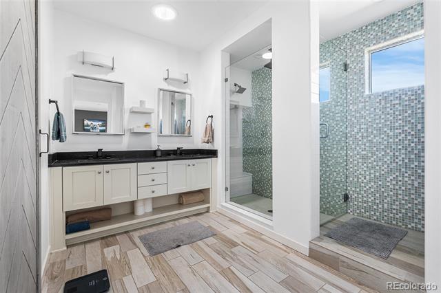 Bright bathroom with a white double vanity and glass showers lined in blue-green mosaic tile.