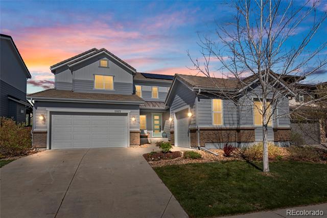Two-story gray house with a double garage and leafless tree at dusk.