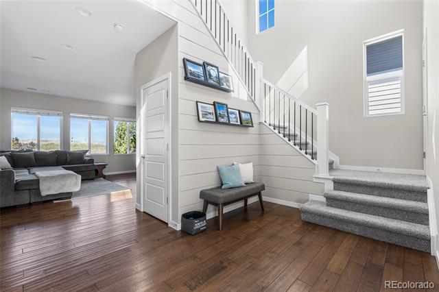 Home entryway with a carpeted staircase, bench, and framed photos; living room visible through the opening.
