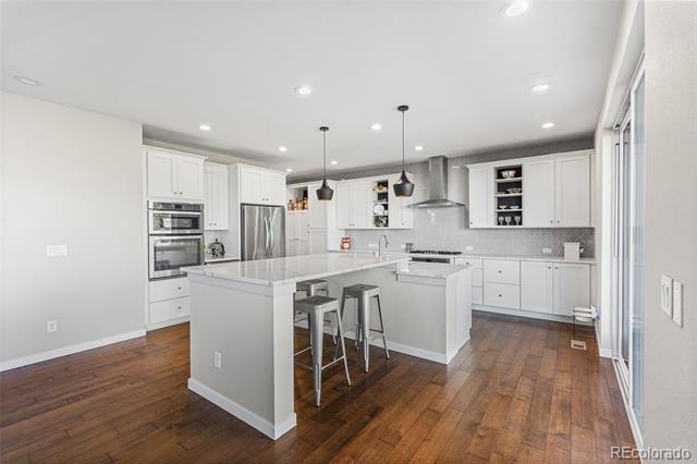 Bright white kitchen with a large island, stainless steel appliances, pendant lights, and warm wood floors.