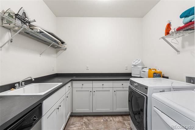 Laundry room with white cabinetry, dark countertops, utility sink, and front-loading washer and dryer.