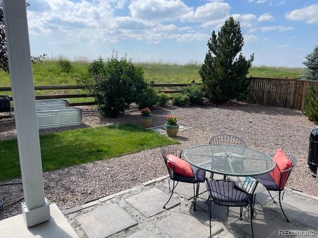Backyard patio with a round glass-top table, cushioned chairs, gravel landscaping, and a pine tree.