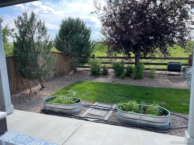 Backyard patio with raised garden beds beside a small lawn and mature trees.
