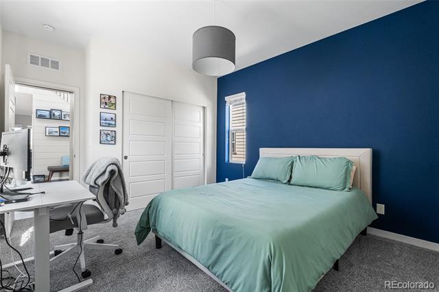 Bedroom with pale teal bedding against a dark blue accent wall, plus a desk and office chair.