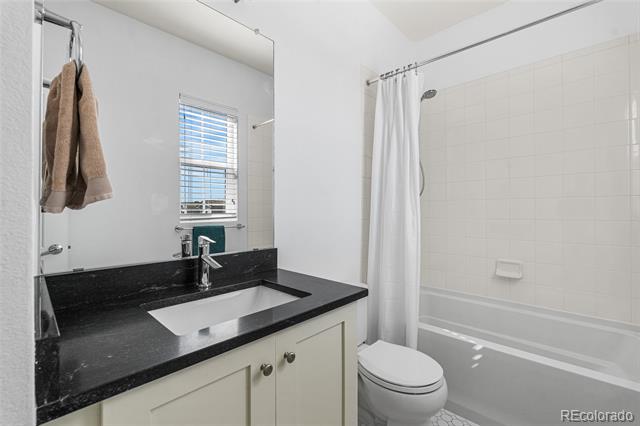 Bathroom with black countertop, white sink vanity, and bathtub with shower curtain.