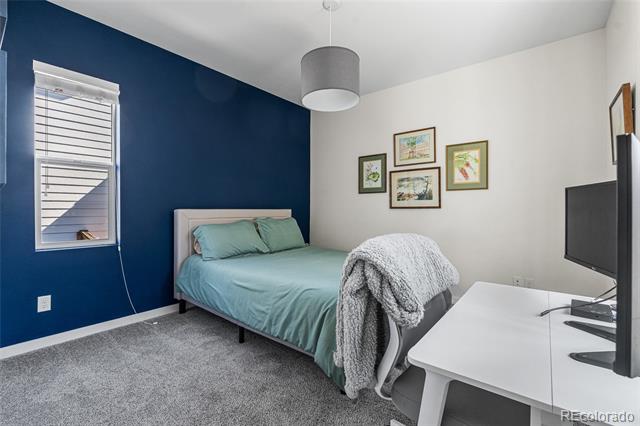 Bedroom with a teal bed, navy accent wall, and white desk beside a television.