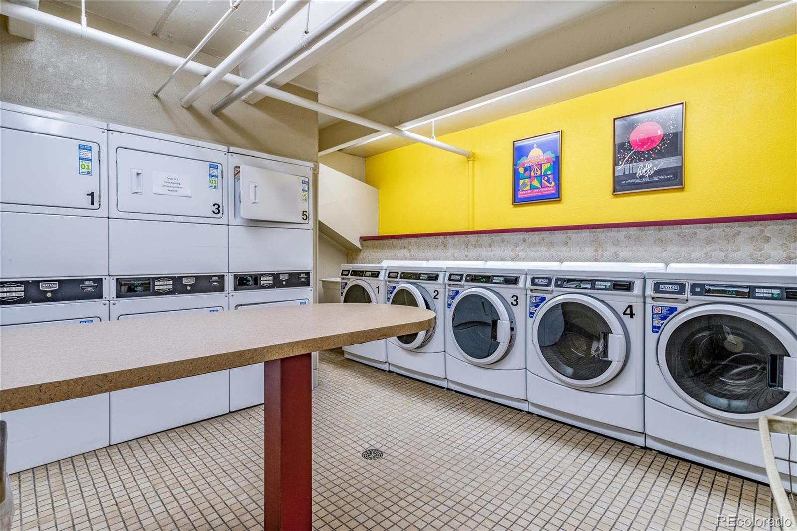 Shared laundry room with commercial washers and dryers and a long folding counter.