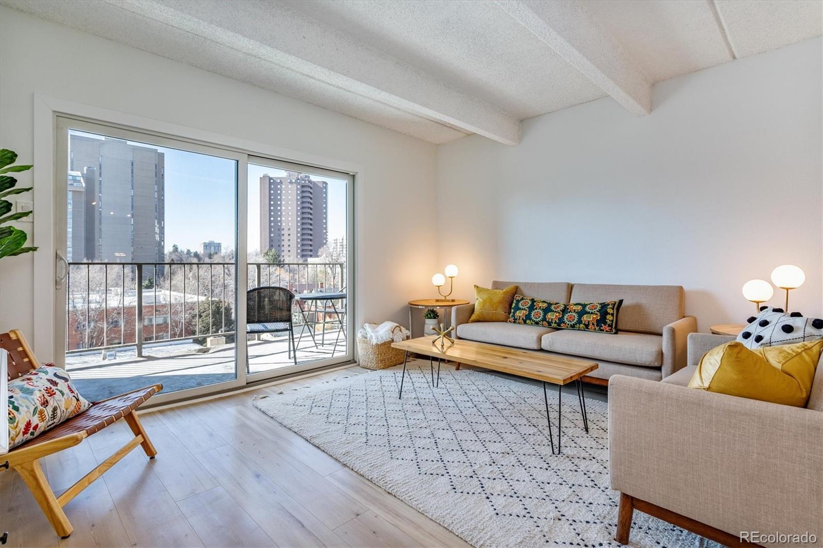 Furnished living room with a balcony, city high-rises, and leafless trees outside.