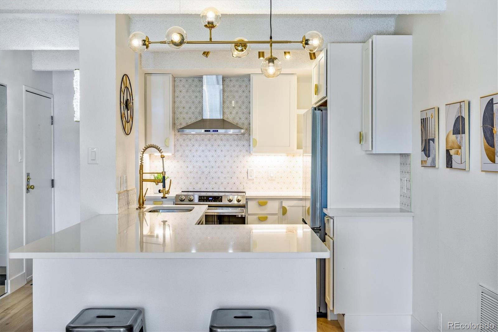 Updated white condo kitchen with a large island, patterned backsplash, stainless appliances, and brass fixtures.