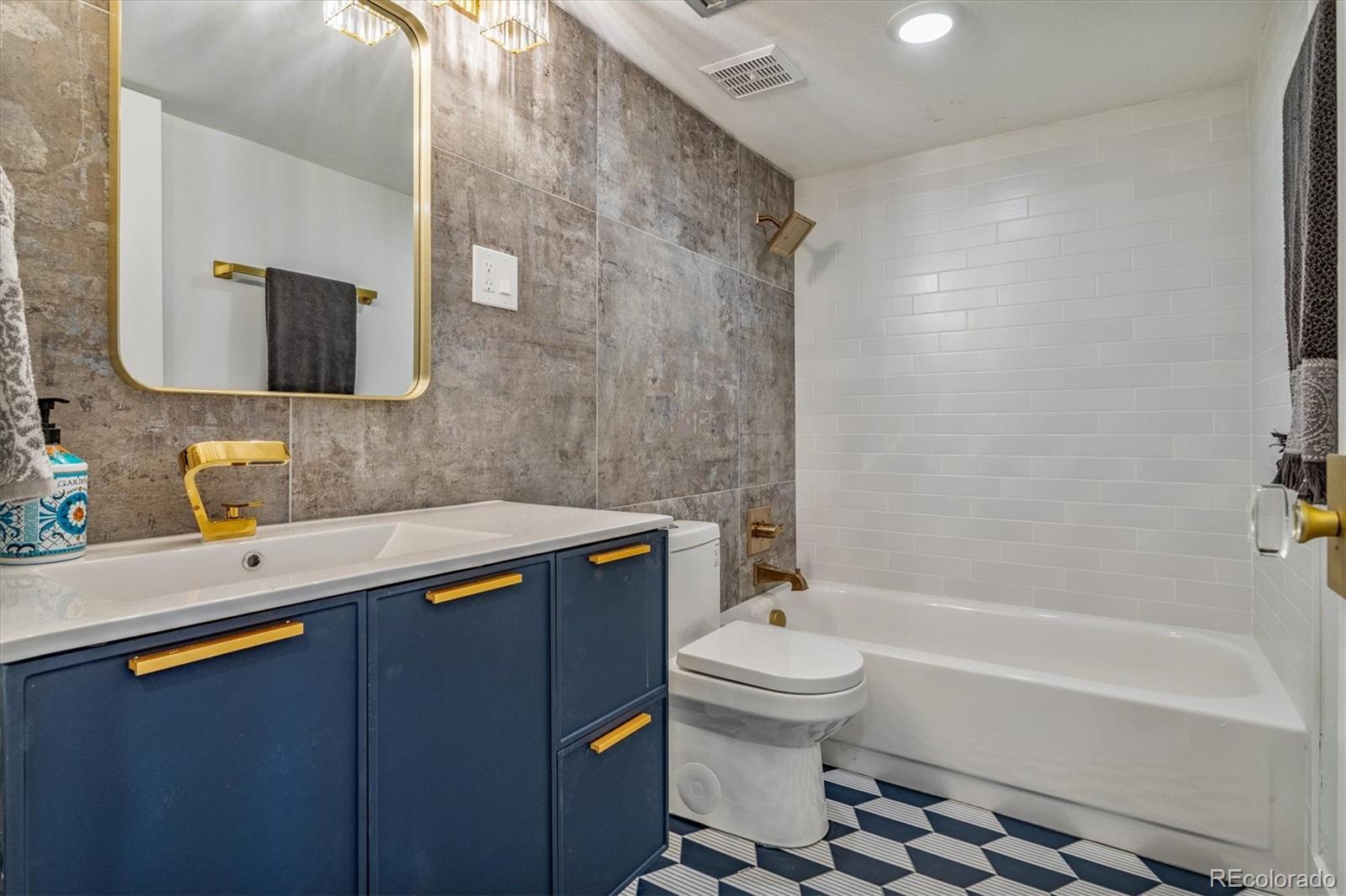 Remodeled bathroom with navy vanity, brass fixtures, gray tile, and a black-and-white geometric floor.