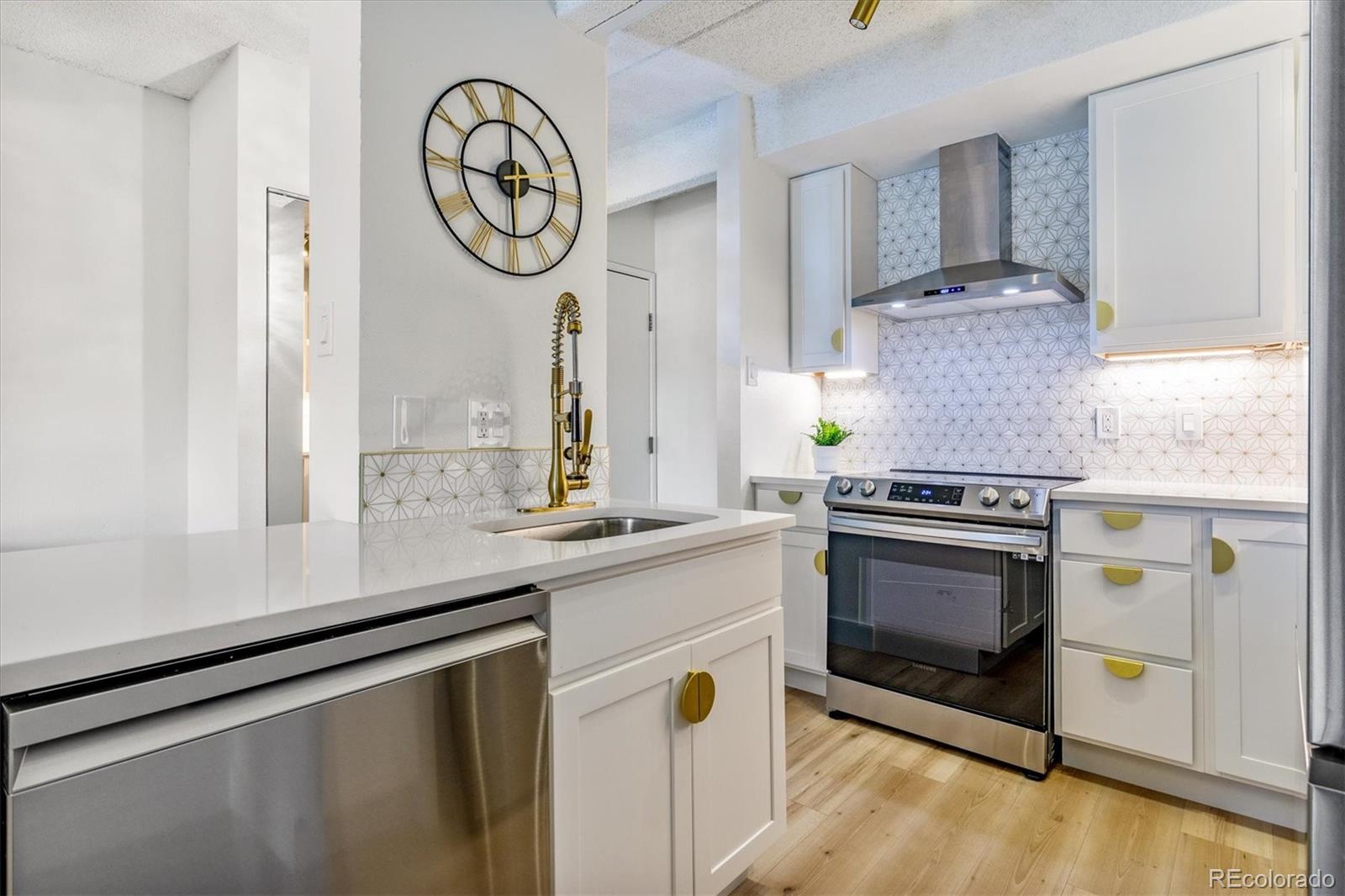 Renovated condo kitchen with a large sink island, gold hardware, patterned backsplash, and stainless steel appliances.