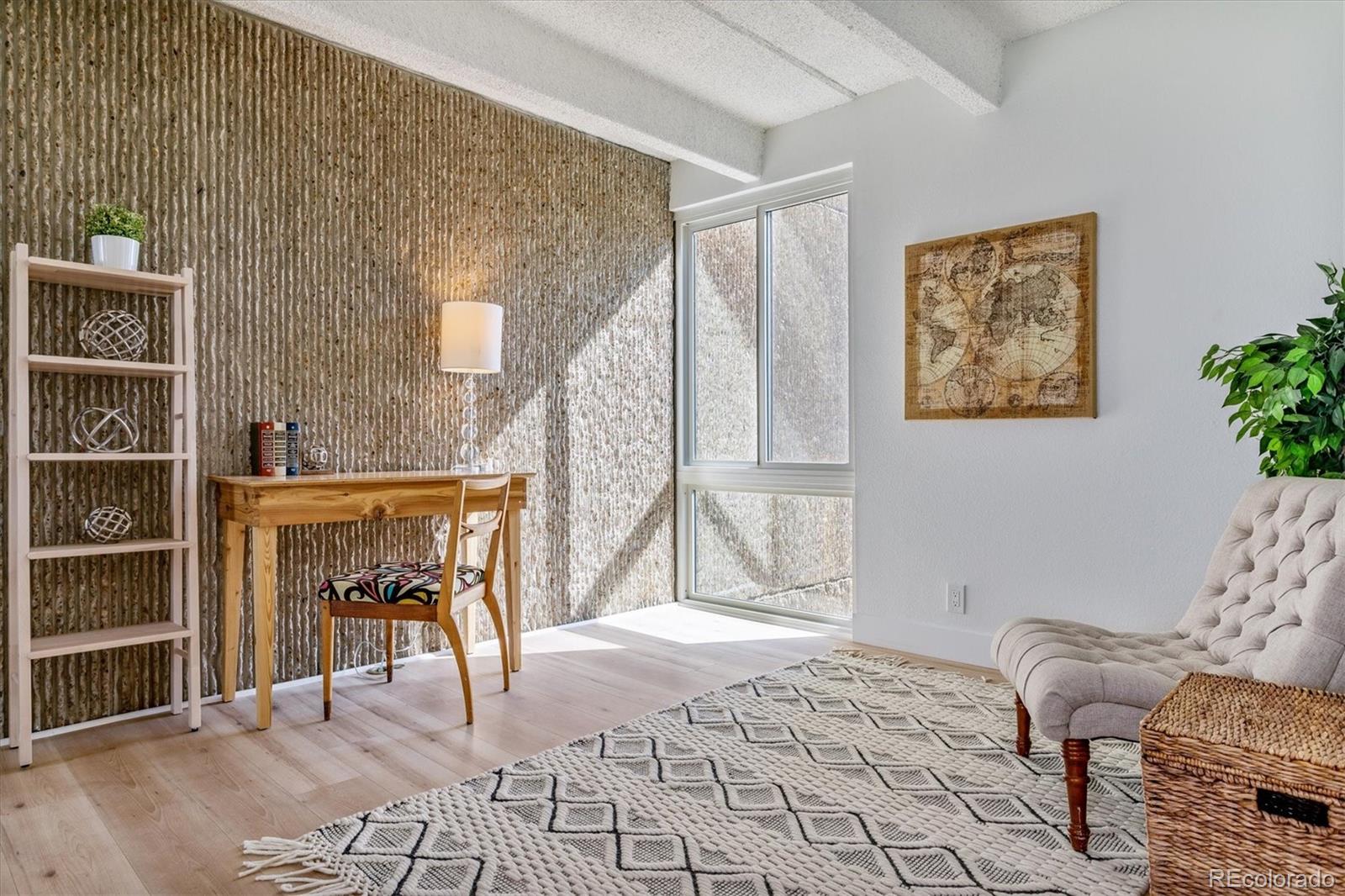 Living room with a textured accent wall, wooden desk, large window, and tufted sofa.