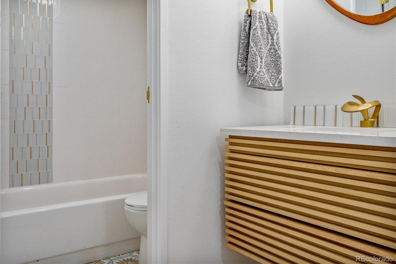 Bathroom with a mosaic tile shower accent, wood-slat vanity, and gold-toned faucet.