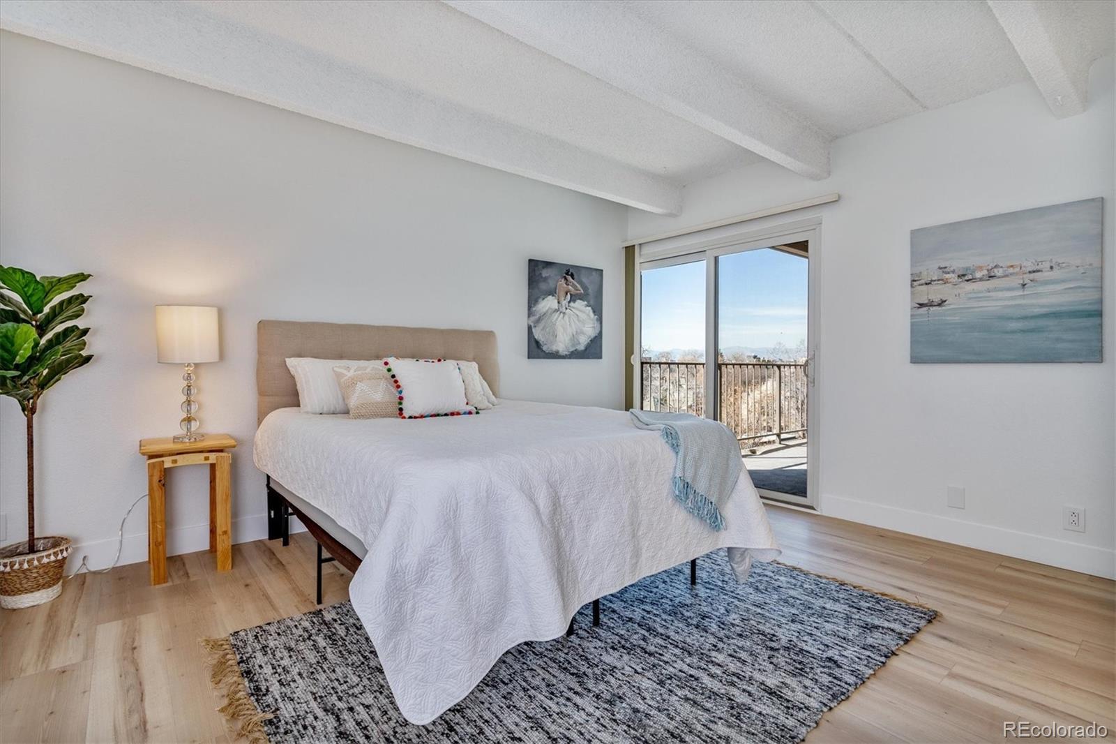 Staged bedroom with a white bed, blue-gray rug, and sliding doors to a balcony.