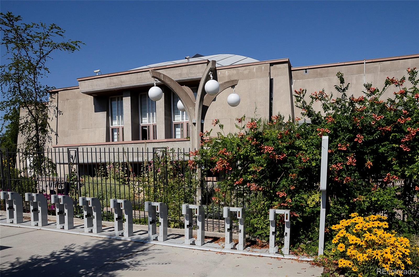 Concrete condominium building with sculptural globe lights, bike racks, and flowering landscaping.
